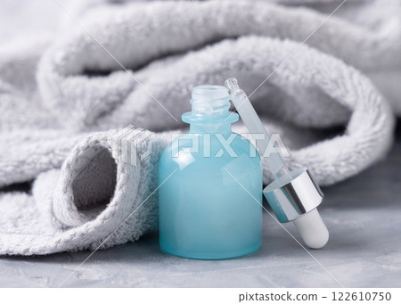 Pipette set near an opened blue dropper bottle near light gray bath towel close up, cosmetic mockup 122610750