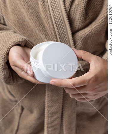 Closeup of woman in brown bathrobe opening white cream jar with hands, cosmetic mockup Closeup of woman in brown bathrobe opening white cream jar with hands, cosmetic mockup 122610764