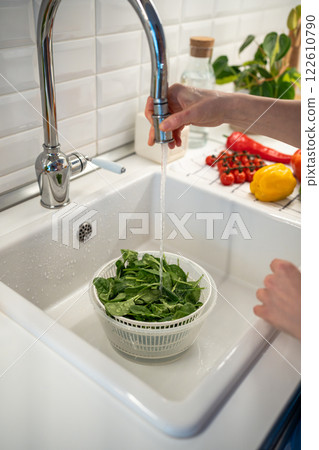 Hand wash fresh spinach leaves in colander under running water in the kitchen sink. Healthy eating. Hand wash fresh spinach leaves in colander under running water in the kitchen sink. Healthy eating. 122610790