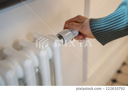 Hand turning radiator valve reducing temperature in flat, private house to save, economize energy 122610792