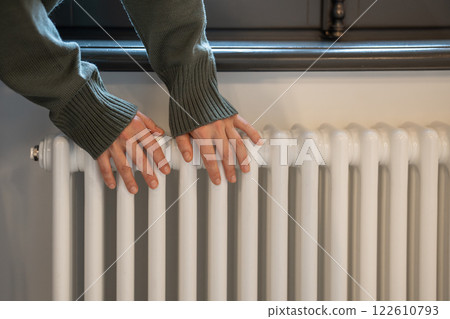 Woman warming hands near radiator at home after walking in cold winter weather, closeup Woman warming hands near radiator at home after walking in cold winter weather, closeup 122610793