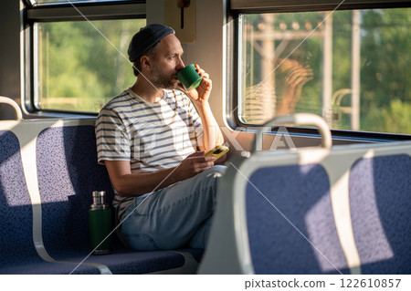 Thoughtful man sips tea from thermos mug while looking out the window during train ride. Thoughtful man sips tea from thermos mug while looking out the window during train ride. 122610857