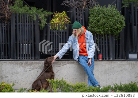 Kind stylish hipster guy in trendy outfit caressing street dog, playing, amusing homeless pet Kind stylish hipster guy in trendy outfit caressing street dog, playing, amusing homeless pet 122610888