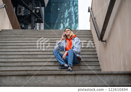 Hipster guy looking like tourist, student, blogger sitting on staircase, speaking on smartphone 122610894