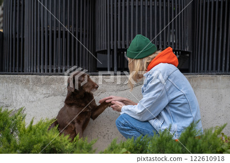 Brown homeless stray dog giving paw to kind guy sitting on haunches in city street, stroking pet Brown homeless stray dog giving paw to kind guy sitting on haunches in city street, stroking pet 122610918