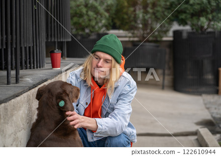 Kind warm-hearted stylish guy in trendy outfit sitting on haunches, caressing street dog with love 122610944