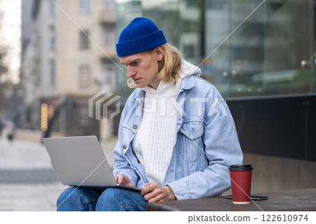 Stylish hipster guy sitting in urban street, working online, searching info in laptop computer 122610974