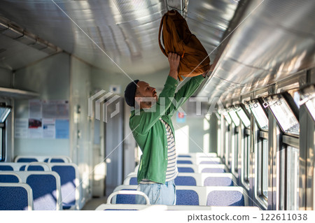 Man tourist lifts backpack onto overhead luggage rack in train. Solo travel and transit convenience 122611038
