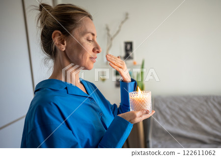 Calm woman enjoy smelling lighted scented candle, meditating, creating cozy atmosphere at home. Calm woman enjoy smelling lighted scented candle, meditating, creating cozy atmosphere at home. 122611062