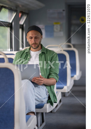 Focused thoughtful man passenger working on laptop while travel by electric train using earphones Focused thoughtful man passenger working on laptop while travel by electric train using earphones 122611070