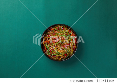 on green background, a black round bowl of rice noodles with striped vegetables sprinkled with sesame seeds, traditional Chinese cuisine 122611406