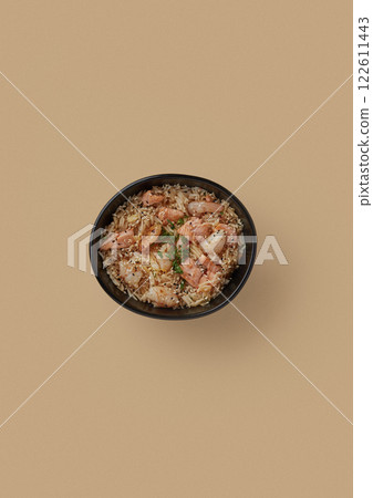 on beige background, a round black plate with fried rice and pieces of tiger shrimp sprinkled with black and white sesame seeds and finely chopped green onions on beige background, a round black plate with fried rice and pieces of tiger shrimp sprinkled with black and white sesame seeds and finely chopped green onions 122611443