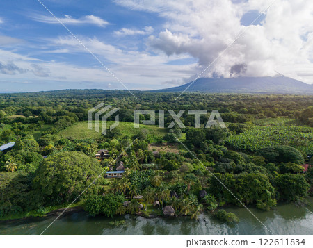 Lush green landscape near volcano with distant clouds and river at midday Lush green landscape near volcano with distant clouds and river at midday 122611834