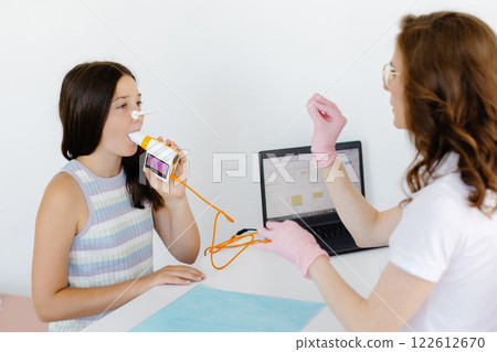 Girl testing breathing function by spirometry in doctors office. Diagnosis of respiratory function in pulmonary disease Girl testing breathing function by spirometry in doctors office. Diagnosis of respiratory function in pulmonary disease 122612670