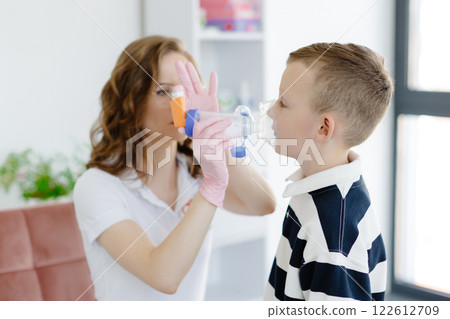 Boy with allergic asthma, inhaling his medication through spacer while sitting in doctors office Boy with allergic asthma, inhaling his medication through spacer while sitting in doctors office 122612709