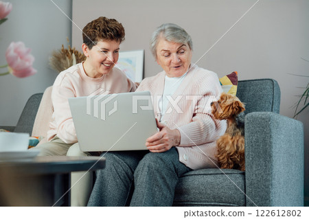 A young woman explaining her senior mother or grandma how to use laptop. Retired lady discovering technology for reading news, chatting with family, watching video, online consulting with doctor. A young woman explaining her senior mother or grandma how to use laptop. Retired lady discovering technology for reading news, chatting with family, watching video, online consulting with doctor. 122612802