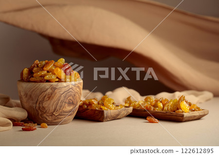 Yellow sultana raisins in a wooden bowl on a beige background. 122612895