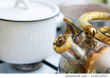 A tea kettle is placed on the stove right next to a pot 122612910