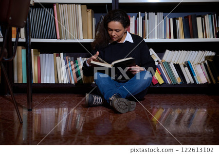 Woman reading a book while sitting on the library floor 122613102