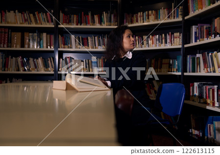 Woman reading a book alone in a quiet library setting Woman reading a book alone in a quiet library setting 122613115
