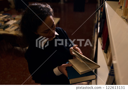 Woman browsing books in a library with a focused expression 122613131
