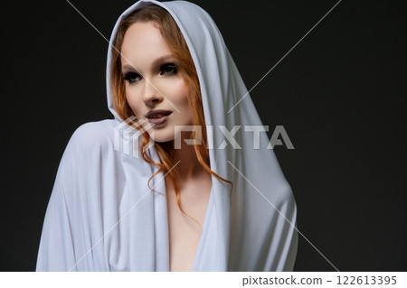 Elegant model in white draped fabric poses gracefully against dark backdrop Elegant model in white draped fabric poses gracefully against dark backdrop 122613395