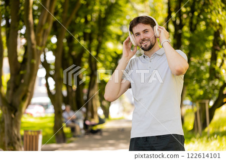 Happy runner jogger smiling man put on wireless headphones earphones enjoy music in park outdoors 122614101