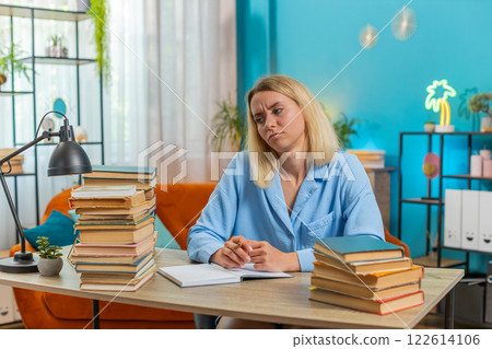 Tired young student writer woman sitting at desk with pile of books writing a novel book with pen 122614106