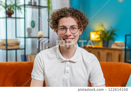 Portrait of happy young Caucasian man sitting on orange sofa looking at camera and smiling at home 122614108