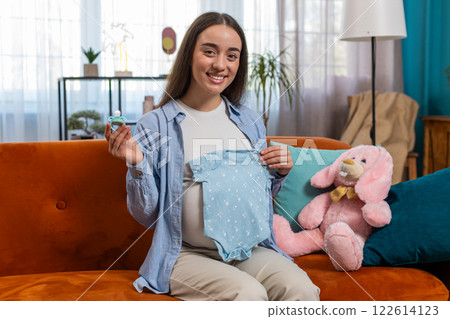 Pregnant woman looking at baby cloth and pacifier, preparing pregnancy, expecting baby, childbirth 122614123