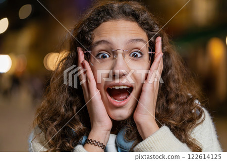Happy teenager girl looking surprised at camera with big open eyes shocked by sudden victory win wow Happy teenager girl looking surprised at camera with big open eyes shocked by sudden victory win wow 122614125