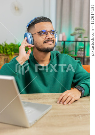 Happy Indian man in wireless headphones dancing listening favorite rock n roll music at home table Happy Indian man in wireless headphones dancing listening favorite rock n roll music at home table 122614183