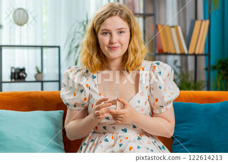 Thirsty young woman sitting at home holding glass of natural aqua make sips drinking still water 122614213