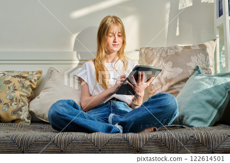 Portrait of female student on couch with digital tablet, studying at home 122614501