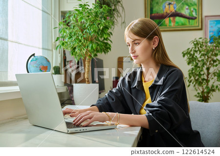 Female teenager college student studying at home sitting at desk typing on laptop 122614524