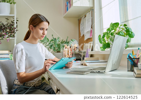 Young teenage girl using graphic tablet for creativity, study, looking at laptop monitor screen Young teenage girl using graphic tablet for creativity, study, looking at laptop monitor screen 122614525