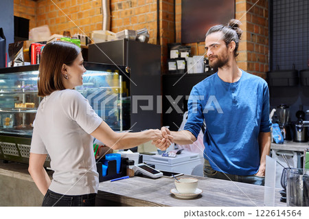 Young man cafe worker shaking hands with woman client customer colleague in coffee shop 122614564