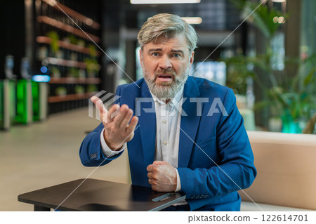 Mature angry boss businessman shouting while looking at camera at modern workplace in office lobby Mature angry boss businessman shouting while looking at camera at modern workplace in office lobby 122614701