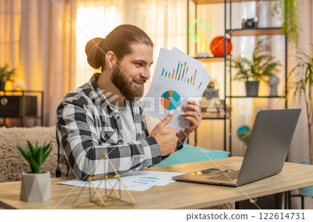 Young man making laptop video chat at home table showing paperwork through webcam positive feedback Young man making laptop video chat at home table showing paperwork through webcam positive feedback 122614731
