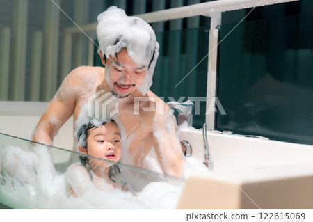 Joyful Asian father and child enjoying bubbly bath time in a modern bathroom setting with bright light 122615069