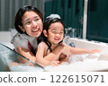 Asian woman and girl are in a bathtub, with the woman smiling and the child laughing. Scene is happy and playful 122615071