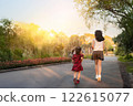 Old sister and young sister running together in the park at sunset. The soft sunlight and natural surroundings create a warm and happy atmosphere, showcasing family bonding and a healthy lifestyle. 122615077