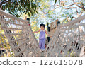 Young Asian Girl Playing on Rope Bridge in Natural Outdoor Setting with Greenery and Bright Sky 122615078