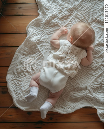 Warm and serene moment with a six month old baby on an antique wood floor with white cotton blanket 122615470