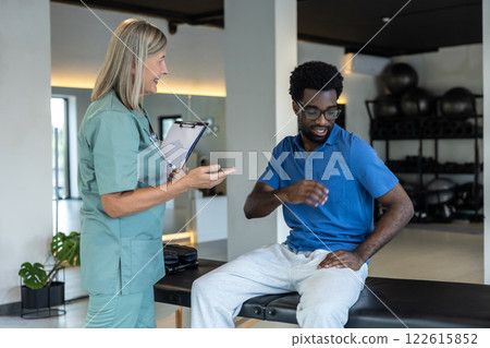 Female physical therapist talking to male patient and making notes Female physical therapist talking to male patient and making notes 122615852