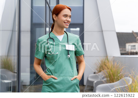 Woman doc with stethoscope wearing uniform friendly smiling while posing in hospital corridor 122615922