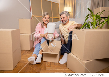 Mature Caucasian couple sitting on floor of new house around cardboard boxes 122615960