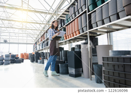 Woman in retail store surrounded with plastic pots for plants on shelves in shop while managing small business 122616096