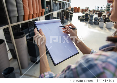 Unrecognizable female worker in plants pot department making notes Unrecognizable female worker in plants pot department making notes 122616104