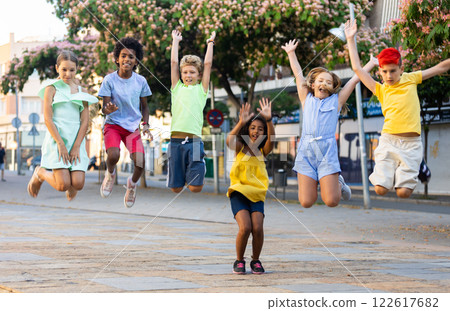 Cheerful tween girls and boys jumping together on summer city street 122617682
